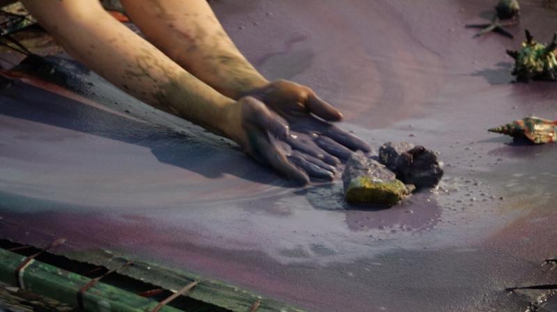 Zwei Hände und einige Steine auf einem Canvas, die Hände werfen Farbe auf die Steine, wie die Wellen auf die Felsen schlagen.