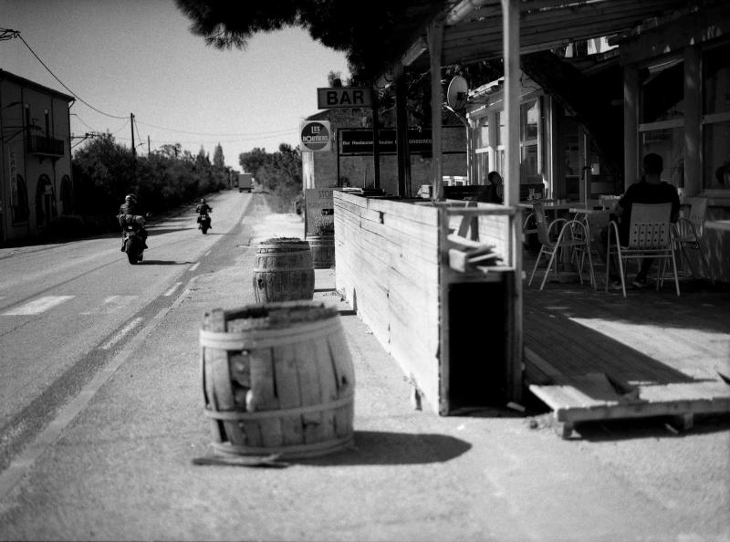Zwei Motorräder fahren auf der Straße vorbei. An der Seite sieht man ein Café-Restaurant. Südfrankreich.