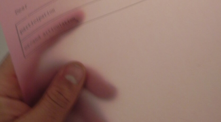 blurred hand holding a transparent pink sheet, a faint label near the top dissolving into motion and softness.